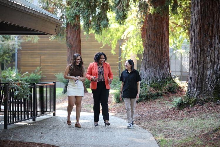 Three women walk on campus and talk to one another
